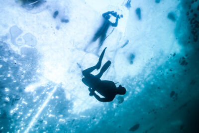 Two divers, one is below the ice